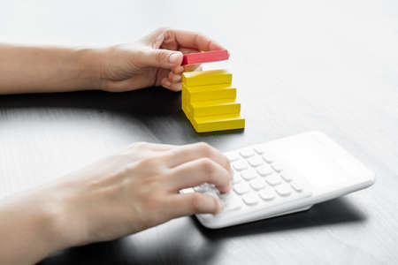 Hands of businesswomen playing wooden block game and have a calculator. Concept Risk of management...