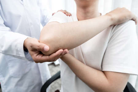 male physiotherapists provide assistance to male patients with elbow injuries to examine patients in rehabilitation centers. Rehabilitation physiotherapy concept.の写真素材