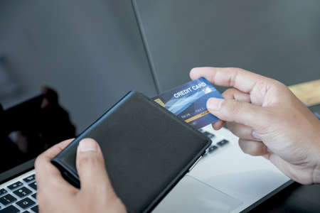 The businessman's hand is holding a credit card and using a laptop for online shopping and internet...