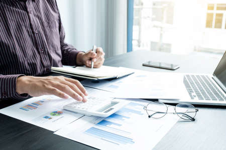 The hands of a male businessman are analyzing and calculating the annual income and expenses in a financial graph that shows results To summarize balances overall in office.の写真素材