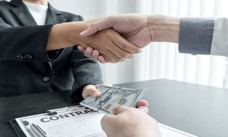 photo of Businessmen shakes hands and dollar note, sign a contract to bribe corruption in the company. The concept of bribery and corruption.の写真素材