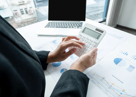 The hands of a male businesswoman use the calculator are analyzing and calculating the annual income and expenses in a financial graph that shows results To summarize balances overall in office.の写真素材