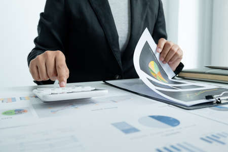 The hands of a male businesswoman use the calculator are analyzing and calculating the annual income...