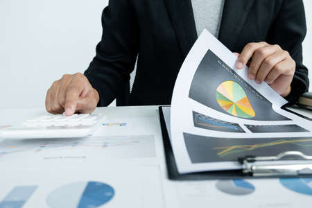 The hands of a male businesswoman use the calculator are analyzing and calculating the annual income and expenses in a financial graph that shows results To summarize balances overall in office.の写真素材