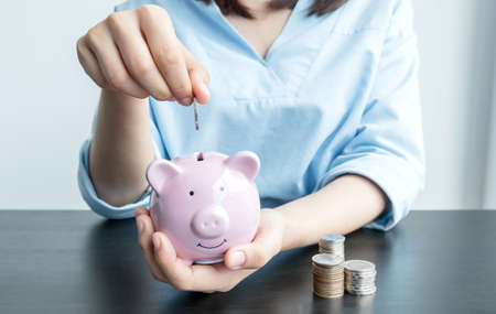 Women's hands are putting coins in the piggy bank Saving money with coins Step into a business that is growing to be successful and save for retirement ideas.の写真素材