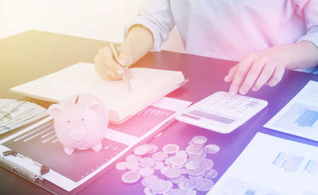 Women's hands count coins, store piggy bank, and using a calculator Calculate graphs to build successful and economical businesses for retirement concepts.の写真素材