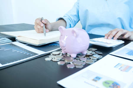 Women's hands count coins, store piggy bank, and using a calculator Calculate graphs to build successful and economical businesses for retirement concepts.の写真素材