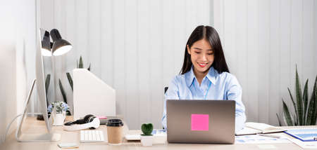 Asian woman working on a laptop with a cheerful and happy smile while working at the office.
