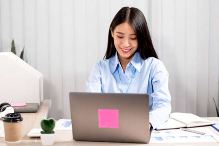 Asian woman working on a laptop with a cheerful and happy smile while working at the office.