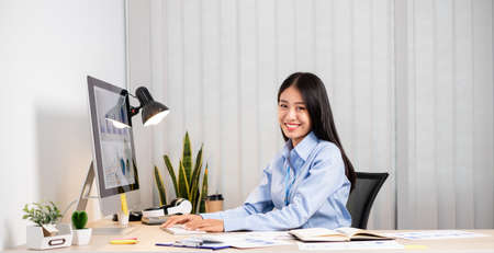 Asian woman working on a laptop with a cheerful and happy smile while working at the office.