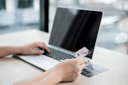 The businesswoman's hand is holding a credit card and using a laptop for online shopping and...