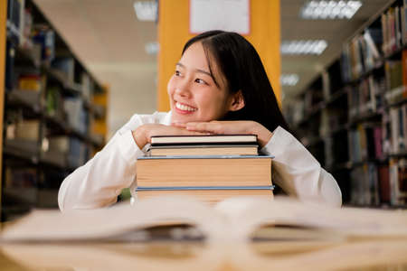 Young Asian women are searching for books and reading from the bookshelves in the college library to...