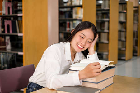 Young Asian women are searching for books and reading from the bookshelves in the college library to research and develop themselves in education.の写真素材