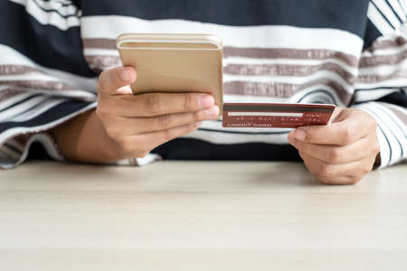 The businesswoman's hand is holding a credit card and using a smartphone for online shopping and...