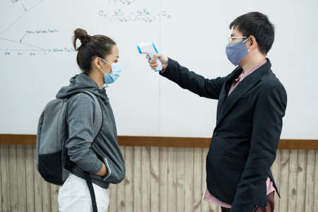 Back to school. Asian male teacher using thermometer temperature screening student for fever against the spread of COVID-19 Before entering the classroom. Virus protection concept.の写真素材