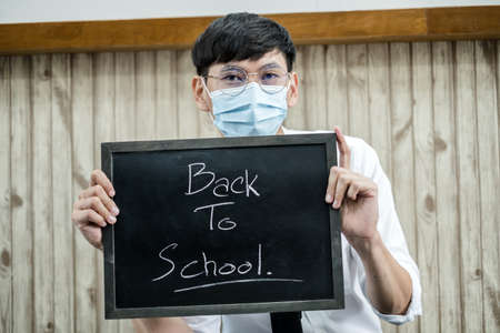 Back to school. Asian male students wearing masks, holding blackboard labeled Back to School. College male Back to School after Pandemic Coronavirus Disease 2019.の写真素材