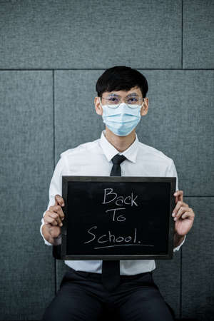 Back to school. Asian male students wearing masks, holding blackboard labeled Back to School....
