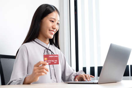 The Asian businesswoman's hand is holding a credit card and using a laptop for online shopping and...