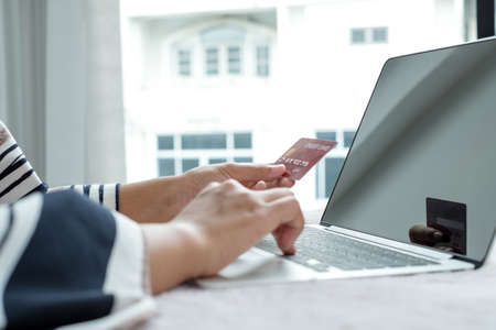 The businesswoman's hand is holding a credit card and using a laptop for online shopping and...