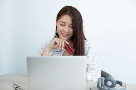 The Asian woman's hand is holding a credit card and using a laptop for online shopping and internet...