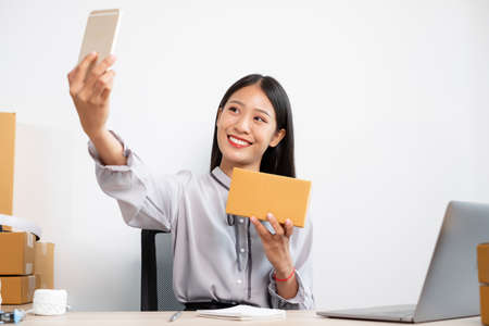 Young Asian woman business owner with many parcel boxes on the table happy online sales job, use...