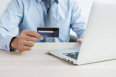 The businessman's hand is holding a credit card and using a laptop for online shopping and internet payment in the office.の写真素材