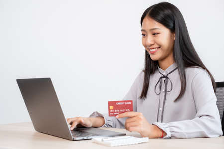 The Asian businesswoman's hand is holding a credit card and using a laptop for online shopping and...