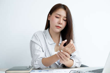 An Asian woman is sitting overtime with her laptop and her wrist aches while working at the office.の写真素材