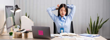 Asian female accountant is tired from working in a chair, stretching to relax and relax while...