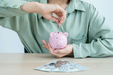 The hand of a businesswoman puts coins in a piggy bank, saves money with coins, steps into a successful growth business, and saves for retirement ideas.の写真素材