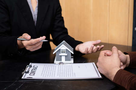A real estate agent with a House model is talking to clients about buying home insurance. Home...