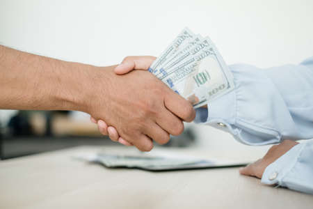 Photo of Businessmen shaking hands and dollar note, sign a contract to bribe corruption in the company. The concept of bribery and corruption.の写真素材