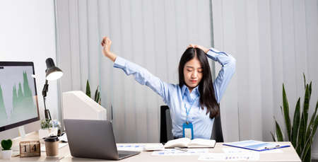Asian female accountant is tired from working in a chair, stretching to relax and relax while...