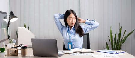 Asian female accountant is tired from working in a chair, stretching to relax and relax while working hard at the office.の写真素材