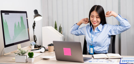 Asian female accountant is tired from working in a chair, stretching to relax and relax while working hard at the office.の写真素材