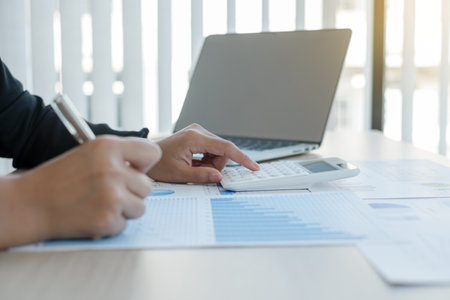 The hand of an accountant woman is analyzing and calculating the financial graph showing the results in the office.の写真素材