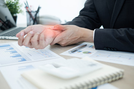 Businessman grasping the painful wrist caused by prolonged work on a laptop keyboard. Wrist numbness Arthritis While working at the office.の写真素材
