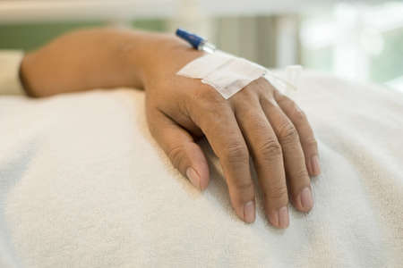 Focus on the hands of the male patient lying on the hospital bed. ready with an injection line or give intravenous medication.の写真素材