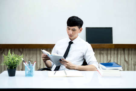 An Asian male teacher at the university is preparing lessons to teach in the classroom.の写真素材