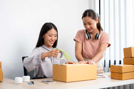 An Asian businesswoman, two owners with lots of boxes on their desks, happy to sell online, take orders from customers, and arrange their mail delivery.の写真素材