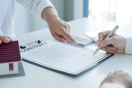 A real estate agent with a house model is talking to clients about buying home insurance and having customers sign contracts under the formal contract agreement. Home rental and insurance concept.の写真素材