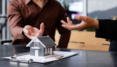 A real estate agent with a House model is talking to clients about buying home insurance. Home insurance concept.