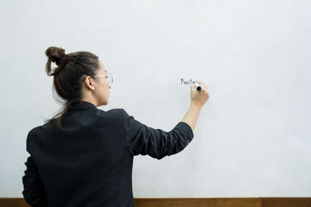 An Asian female teacher in a classroom near the whiteboard is writing and teaching a lesson with a special lecture in a class column. Math teacher explains arithmetic sums to university students.の写真素材