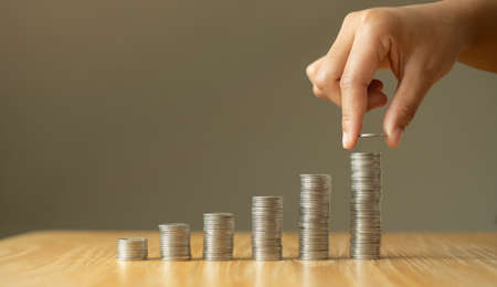 Woman's hand. Place a coin on the coin graph with coins, saving money with coins, stepping into a successful growing business, and saving for thought in retirement. Retirement savings concept.の写真素材