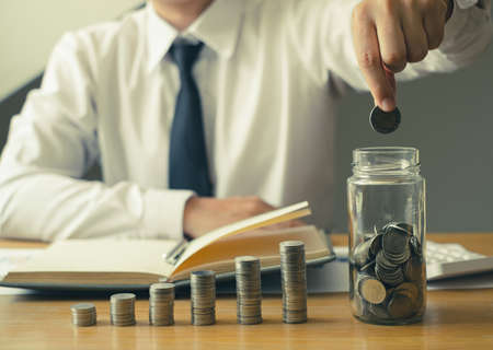 Man's hand. Put a coin into a glass bottle with coins, saving money with coins, stepping into a...
