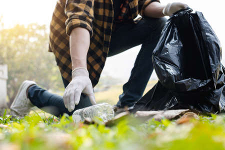 Man's hands pick up plastic bottles, put garbage in black garbage bags to clean up at parks, avoid pollution, be friendly to the environment and ecosystem.の写真素材