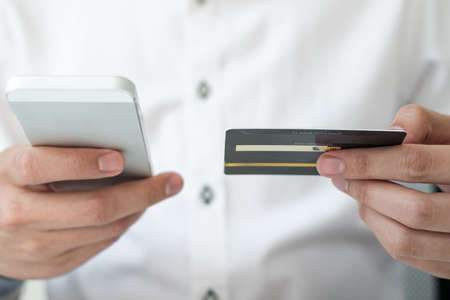 The businessman's hand is holding a credit card and using a smartphone for online shopping and...