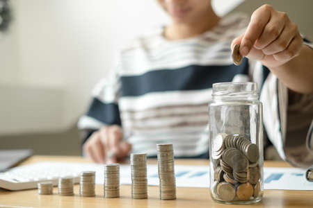 Woman's hand. Put a coin into a glass bottle with coins, saving money with coins, stepping into a...