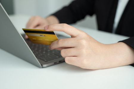 The businesswomen's hand is holding a credit card and using a laptop for online shopping and...