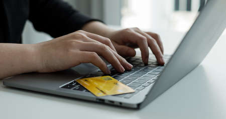 The businesswomen's hand is holding a credit card and using a laptop for online shopping and...